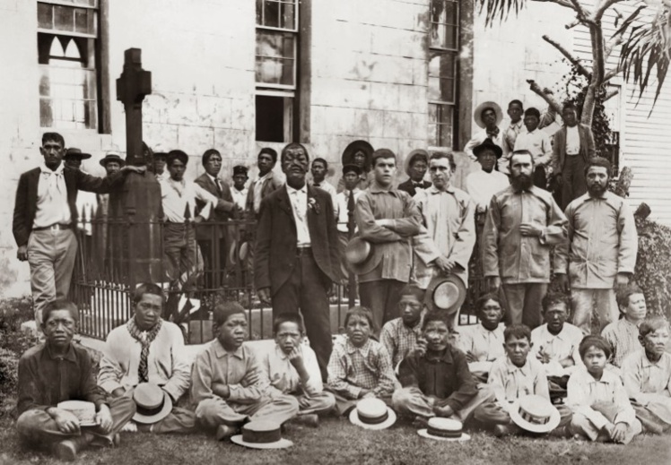 Deux missionnaire (à droite du cliché) et les lépreux de Kalawao autour de la tombe de Damien, qui reposa 47 ans sur son île, avant que son corps ne soit rapatrié en Belgique. Deux missionnaire (à droite du cliché) et les lépreux de Kalawao autour de la tombe de Damien, qui reposa 47 ans sur son île, avant que son corps ne soit rapatrié en Belgique.