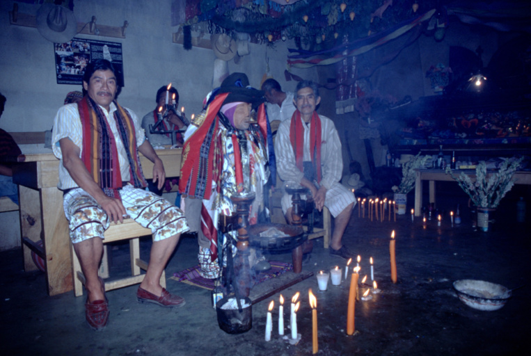 On le remarque sur ce cliché, les deux grands prêtres assis entourant Maximon ne sont pas seuls ; d’autres prêtres moins gradés (mais grands buveurs eux aussi) se tiennent derrière eux. On le remarque sur ce cliché, les deux grands prêtres assis entourant Maximon ne sont pas seuls ; d’autres prêtres moins gradés (mais grands buveurs eux aussi) se tiennent derrière eux.