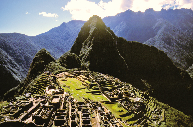 Vue classique, depuis  les hauteurs de la cité, du Machu Picchu (les ruines) et du Huayna Picchu (le “Jeune pic”). Au sommet, des grottes étaient consacrées au culte de la lune. L’ascension est à éviter absolument si l’on est sujet au vertige...