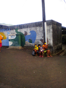 Des enfants attendent le bus scolaire, assis par terre et sans protection