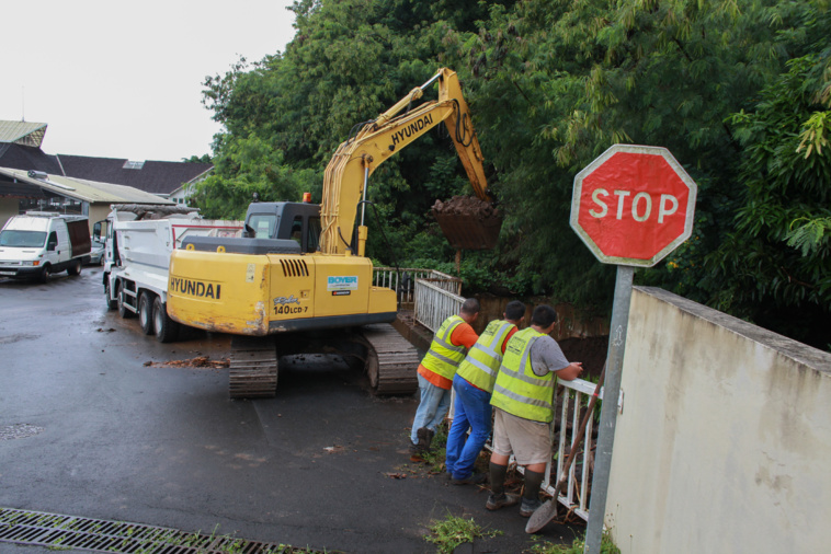 Les ouvriers en train de curer le caniveau d’évacuation des eaux de pluie. Crédit photo : Greg Boissy. Les ouvriers en train de curer le caniveau d’évacuation des eaux de pluie. Crédit photo : Greg Boissy.