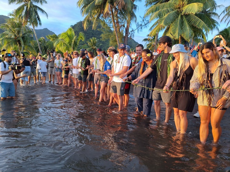 Surfeurs et officiels réunis sur la plage lors de la cérémonie de l’eau, une longue tresse de ‘autῙ dans les mains. Surfeurs et officiels réunis sur la plage lors de la cérémonie de l’eau, une longue tresse de ‘autῙ dans les mains.