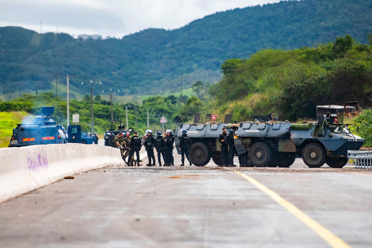 DELPHINE MAYEUR / AFP. Des véhicules blindés de la gendarmerie française montent la garde sur la RT1, sécurisant une machine qui débarrasse la route de débris et d'ordures dans la commune de Paita, en Nouvelle-Calédonie, le 19 mai.