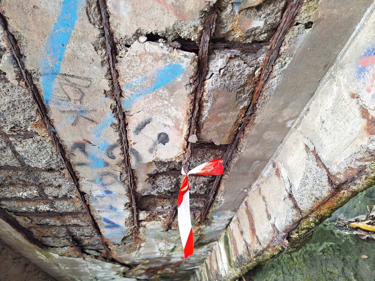 Sous l’escalier, le béton s’effrite et des fers sont apparents.