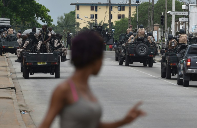 Une femme regarde les soldats ivoiriens qui patrouillent près du quartier général de l'armée, le camp militaire de Gallieni, à Abidjan le 12 mai 2017 (AFP / ISSOUF SANOGO)
