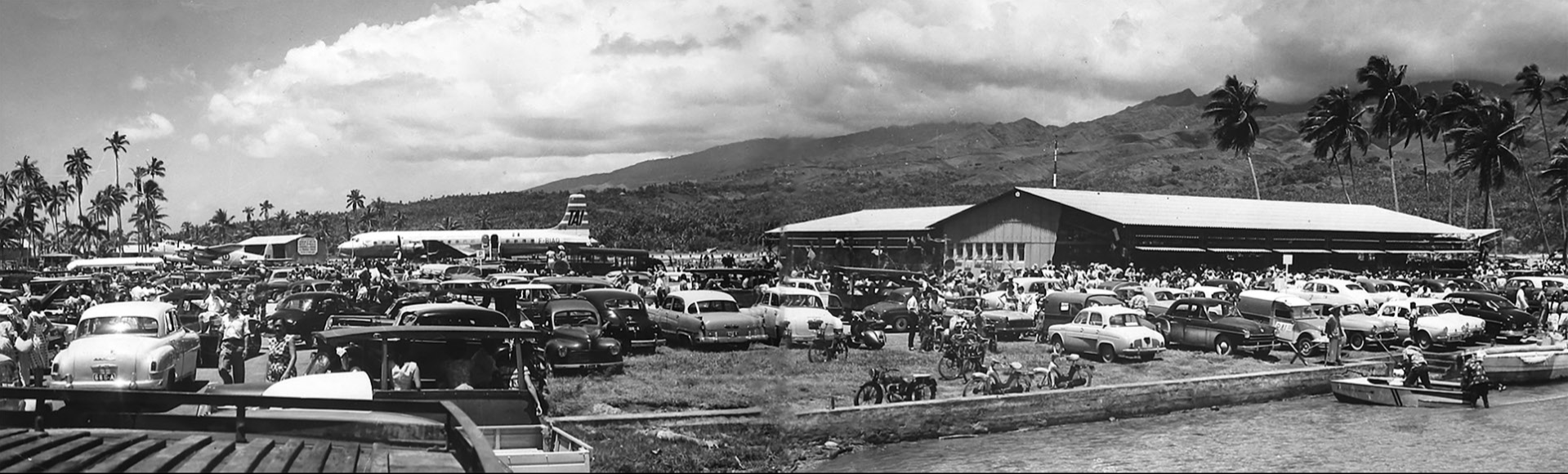Sur le motu Tahiri, un exceptionnel rassemblement populaire accueille le DC 7C, premier avion commercial à s’être posé sur l’île en ce jour historique du 16 octobre 1960. À l’écart, à gauche de l’image, près des cocotiers, le Lancaster de la 9S de la Tontouta dont la mission est de photographier les atolls du sud des Tuamotu. Certains seront choisis comme bases du Centre d’expérimentations atomiques durant les trente-cinq années suivantes.