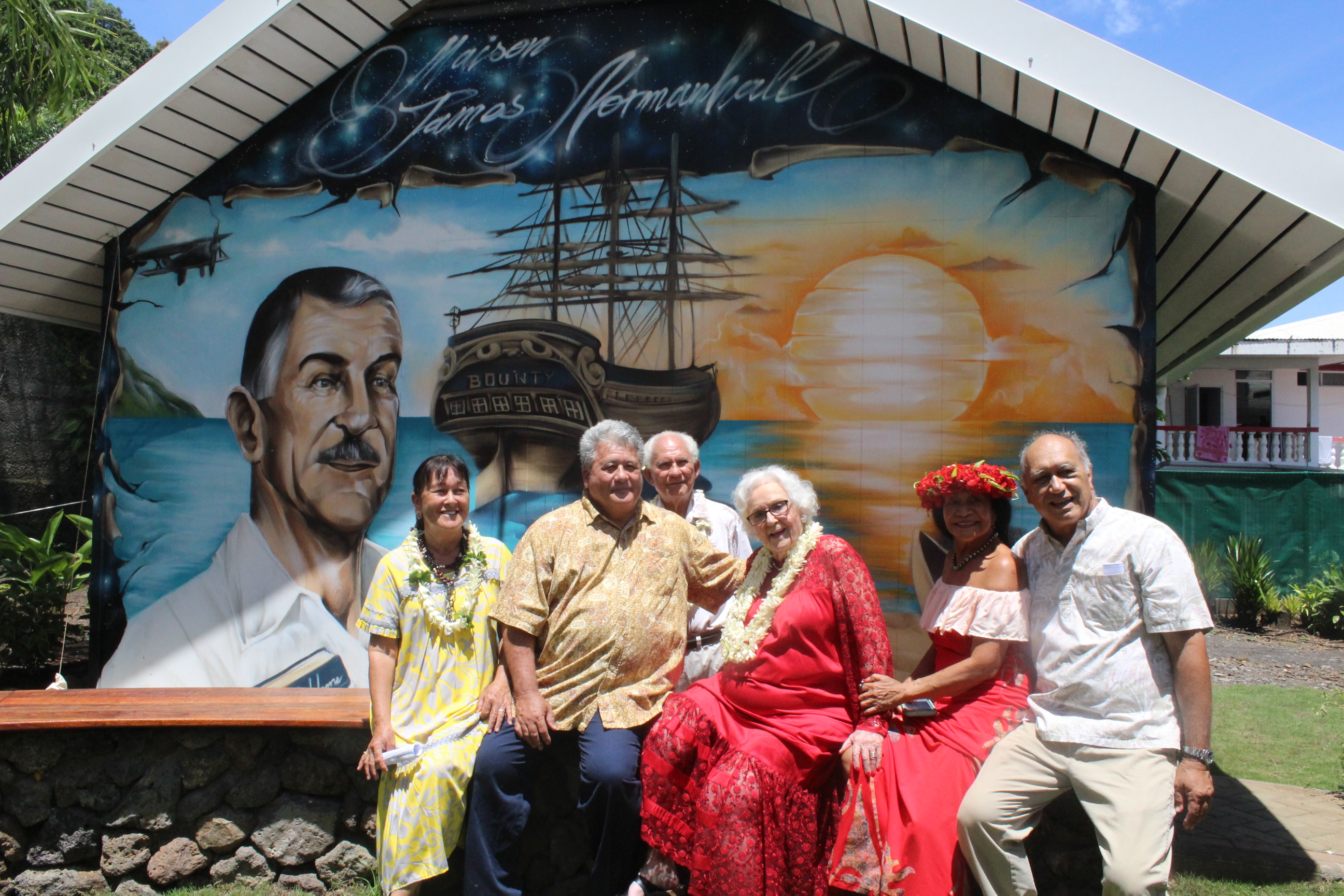 Nancy Hall-Rutgers, en robe rouge, entourée de ses proches devant la fresque représentant son père, James Norman Hall.