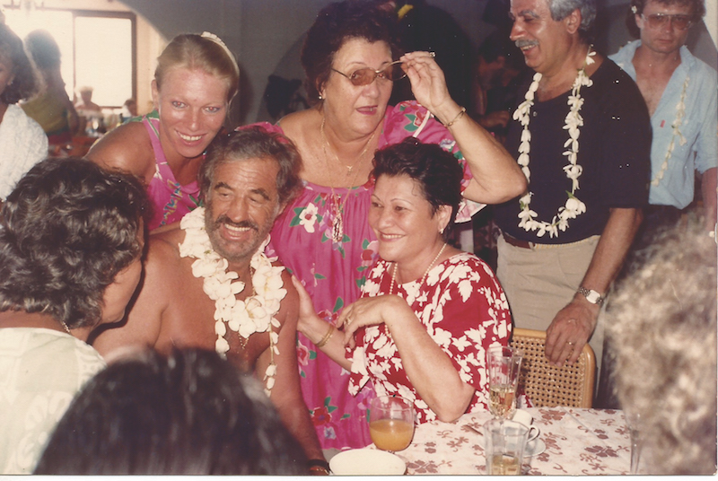 Greta Nenon en robe rouge à fleurs et Jean-Paul Belmondo, en tee-shirt noir Charly Kouberessian maquilleur attitré de Belmondo. (Photo : Michel Darius, collection Greta Nenon)