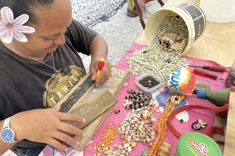 Hina en train de piquer les coquillages pour réaliser une parure de bijoux.