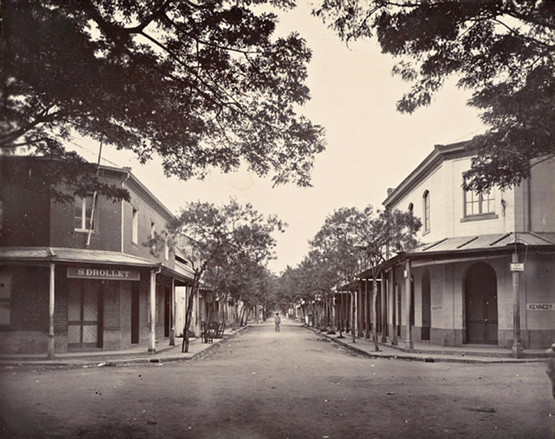La rue de la Petite-Pologne en 1900. A gauche le magasin général en briques de Sosthène Drollet, l’inventeur de la gelée de goyave, qui est devenue en 1938 la pharmacie Jacquier. Photo Holmes