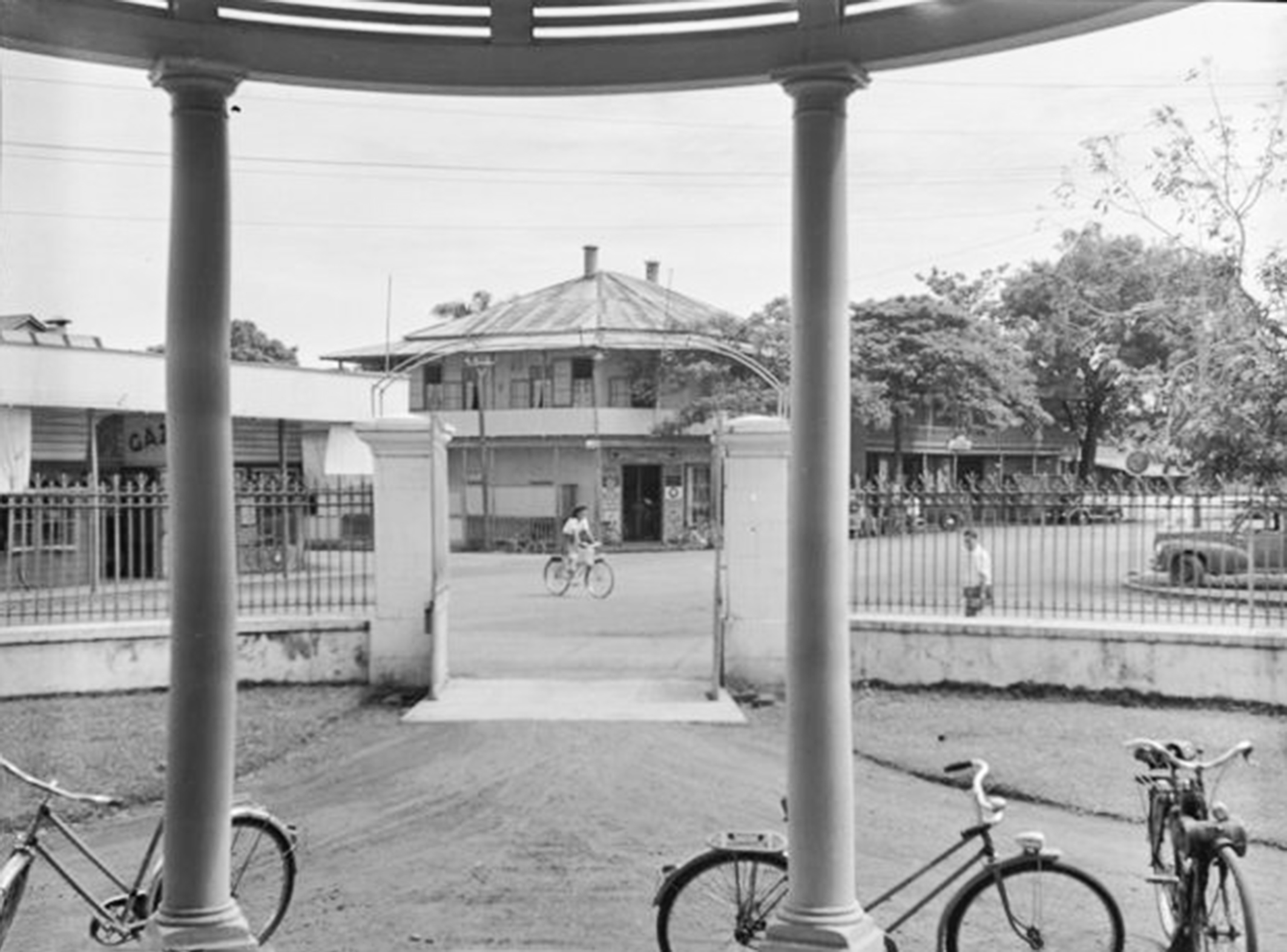 La place de la cathédrale en 1952 vue de l’entrée de la banque d’Indochine, avec en face la construction en bois à l’emplacement de l’actuelle pharmacie de la cathédrale. Photo Whites Aviation